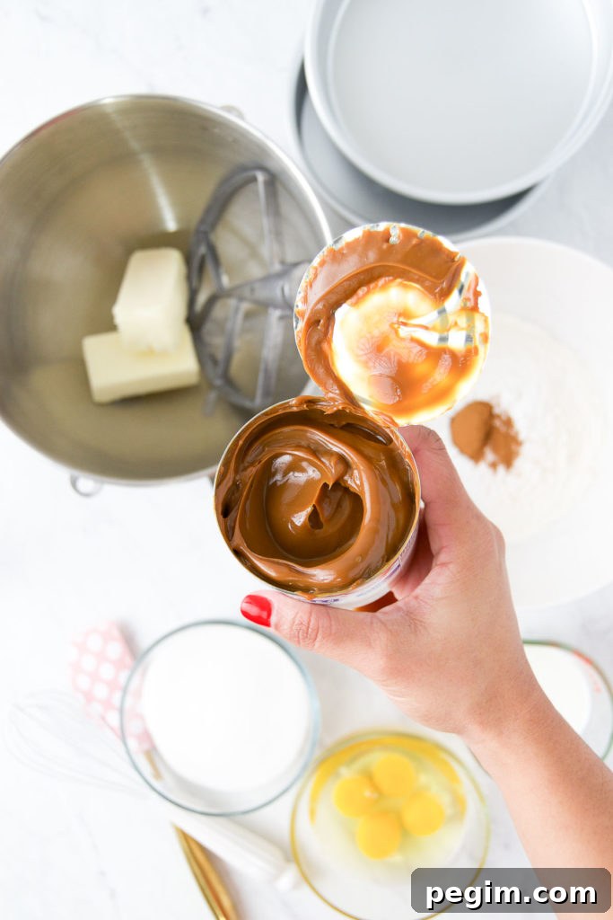 Cinnamon Churro Cake with Crispy Sugar Crust 5 A hand holds an open can of La Lechera dulce de leche above cake ingredients in bowls