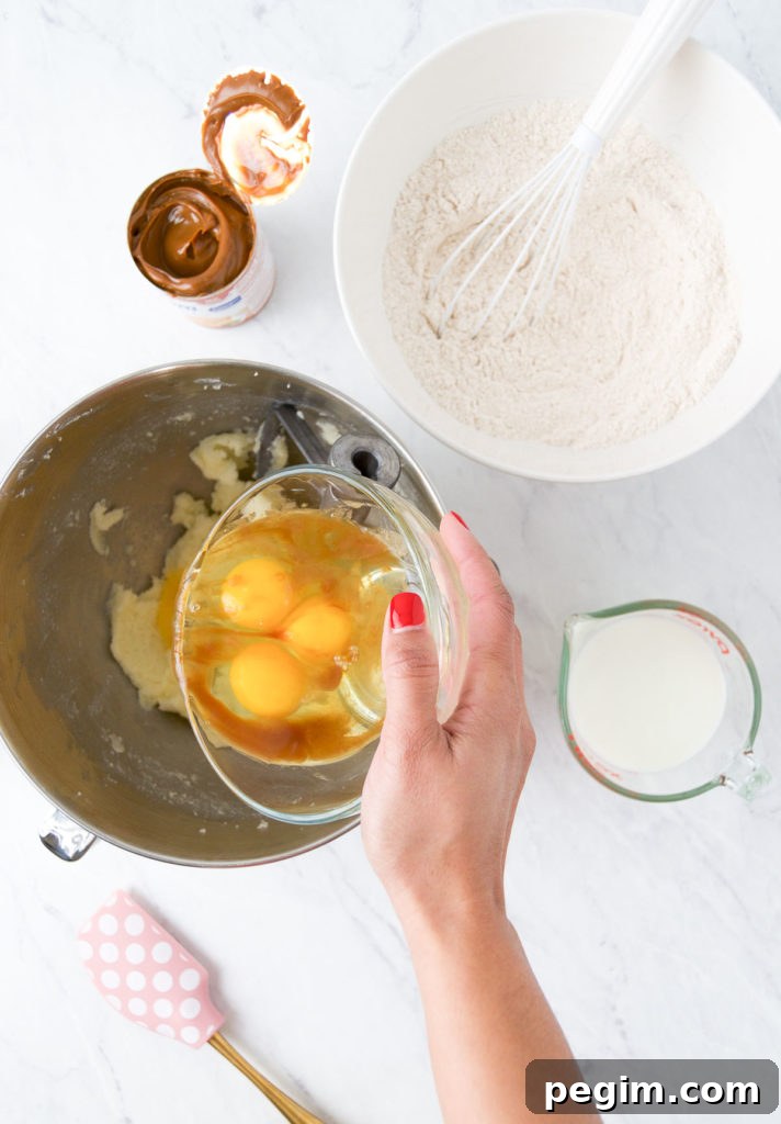 Cinnamon Churro Cake with Crispy Sugar Crust 7 A hand pours eggs into a bowl holding creamed butter and sugar