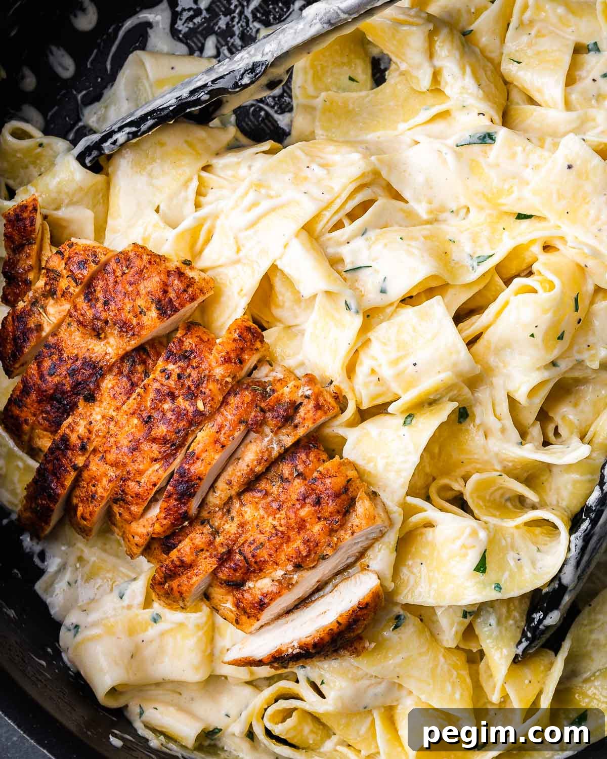 Creamy Chicken Alfredo Pasta Recipe 4 Chicken alfredo pasta in black pan with tongs.