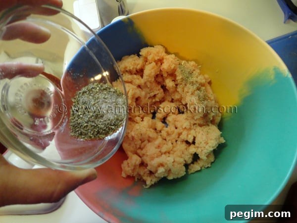 homemade-chicken-nuggets-step-4 A photo of salt, pepper, onion powder, oregano and parsley seasoning being poured over raw chicken in a bowl.