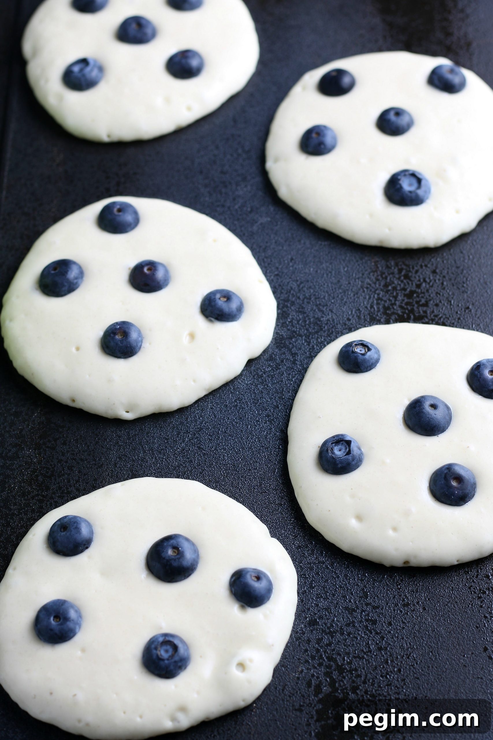 Fluffy Homemade Blueberry Pancakes 6 blueberry pancakes on a griddle