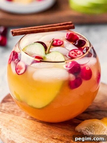 Glass of apple cider punch on wood cutting board with lemon slice.
