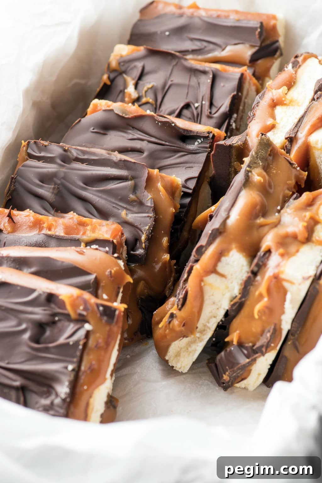 A box of caramel and chocolate topped shortbread nestled in white parchment paper