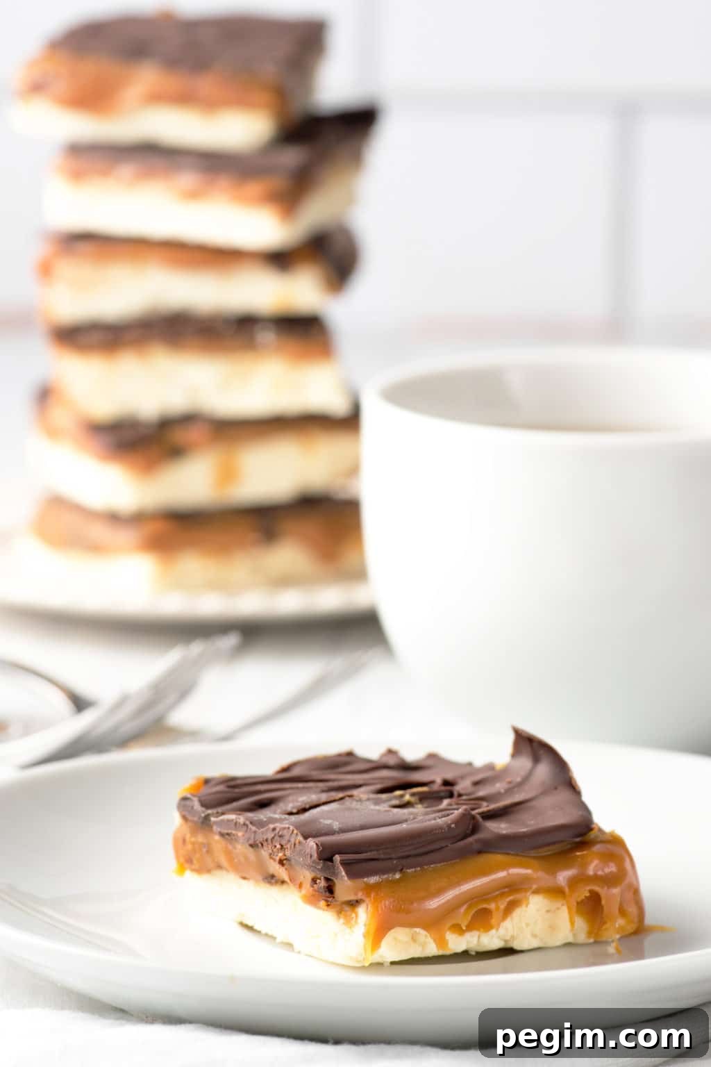 A single low carb millionaire square on a white plate with a stack of squares and coffee cup in the background.