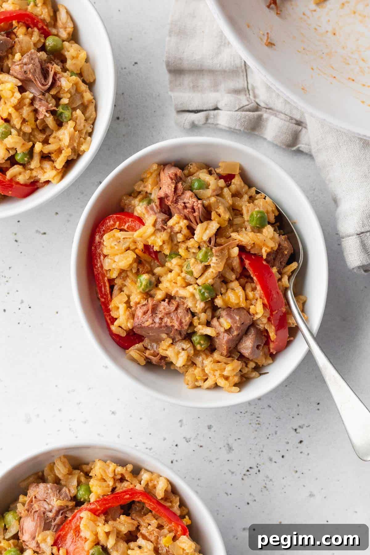 Vegan Arroz a la Valenciana: Spanish-Style Rice with Vegetables 9 Valencian style rice in a bowl with a silver spoon, with 2 more bowls in the corners of the shot.