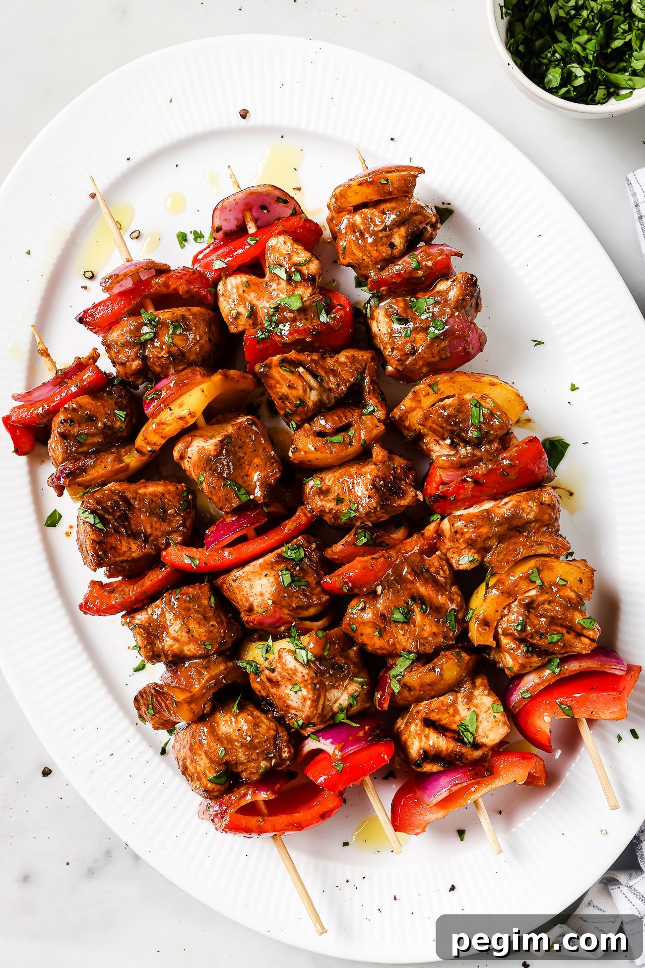 An overhead view of four chicken kabobs on a white serving plate.