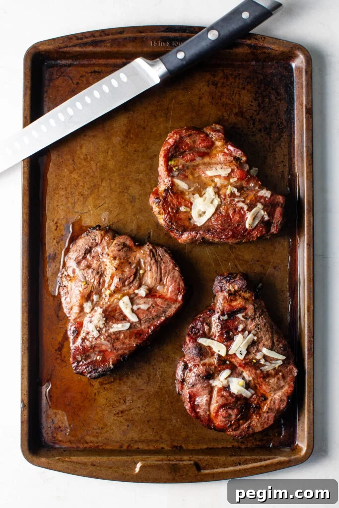 grilled pork coppa steaks topped with garlic on a sheet pan