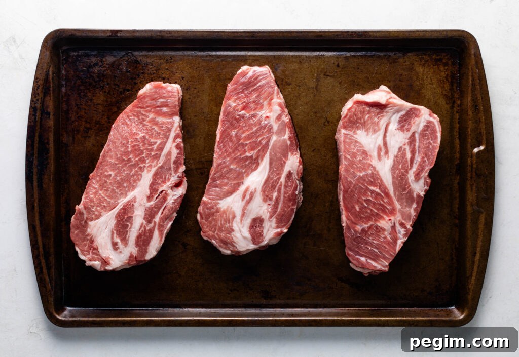 three raw pork coppa steaks on a sheet pan